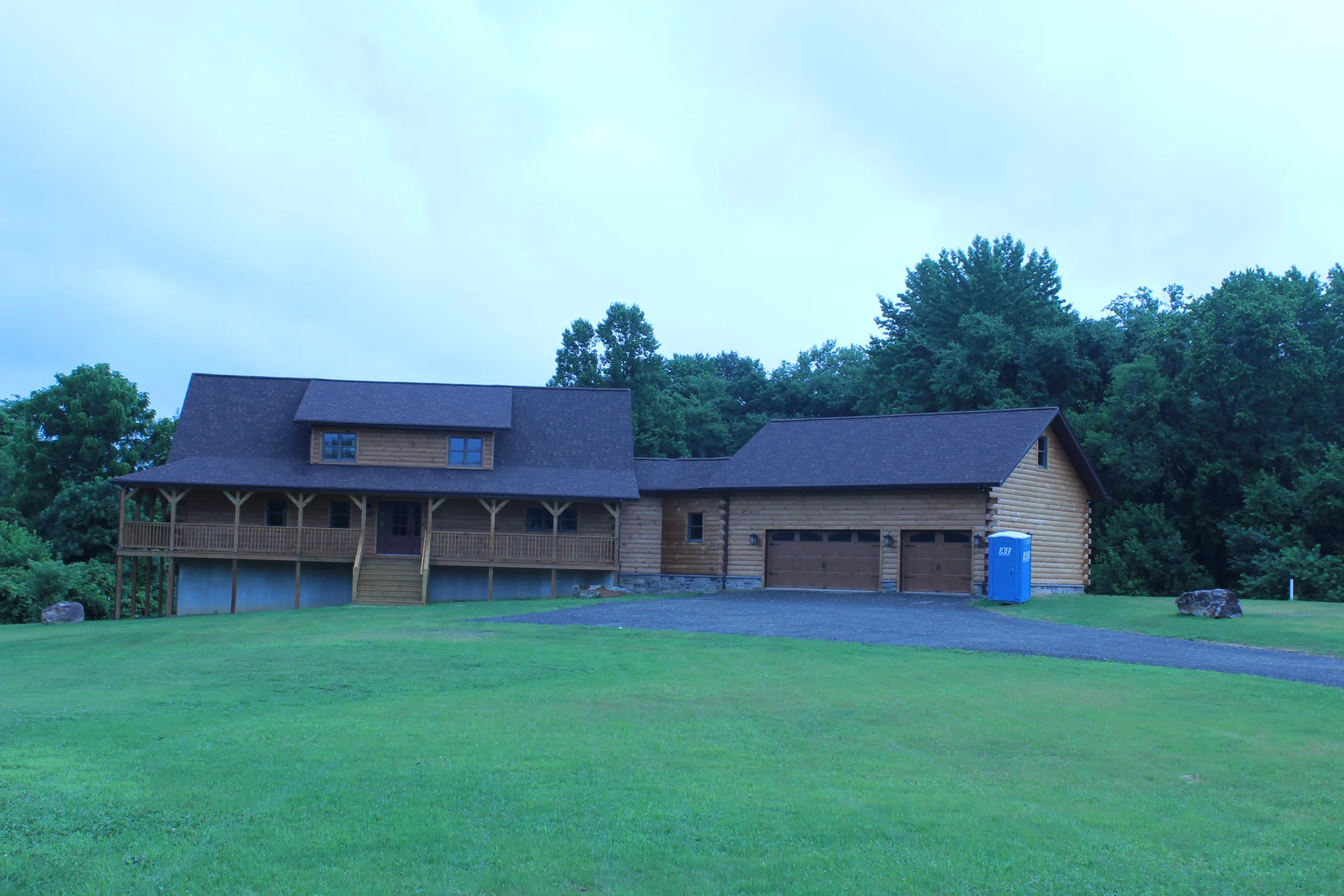A large log home with a garage in the middle of a grassy field.